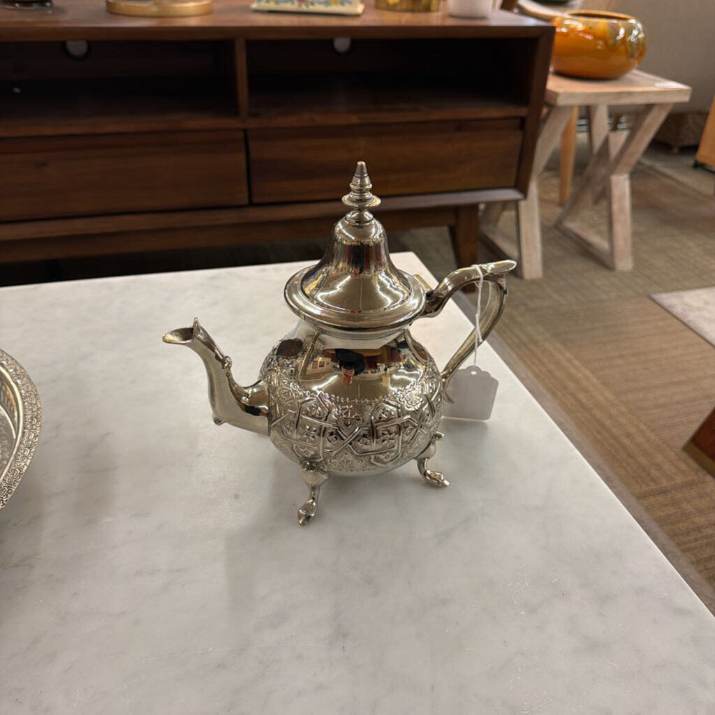 Silver teapot on a marble surface with a wooden cabinet in the background