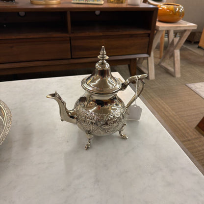 Silver teapot on a marble surface with a wooden cabinet in the background