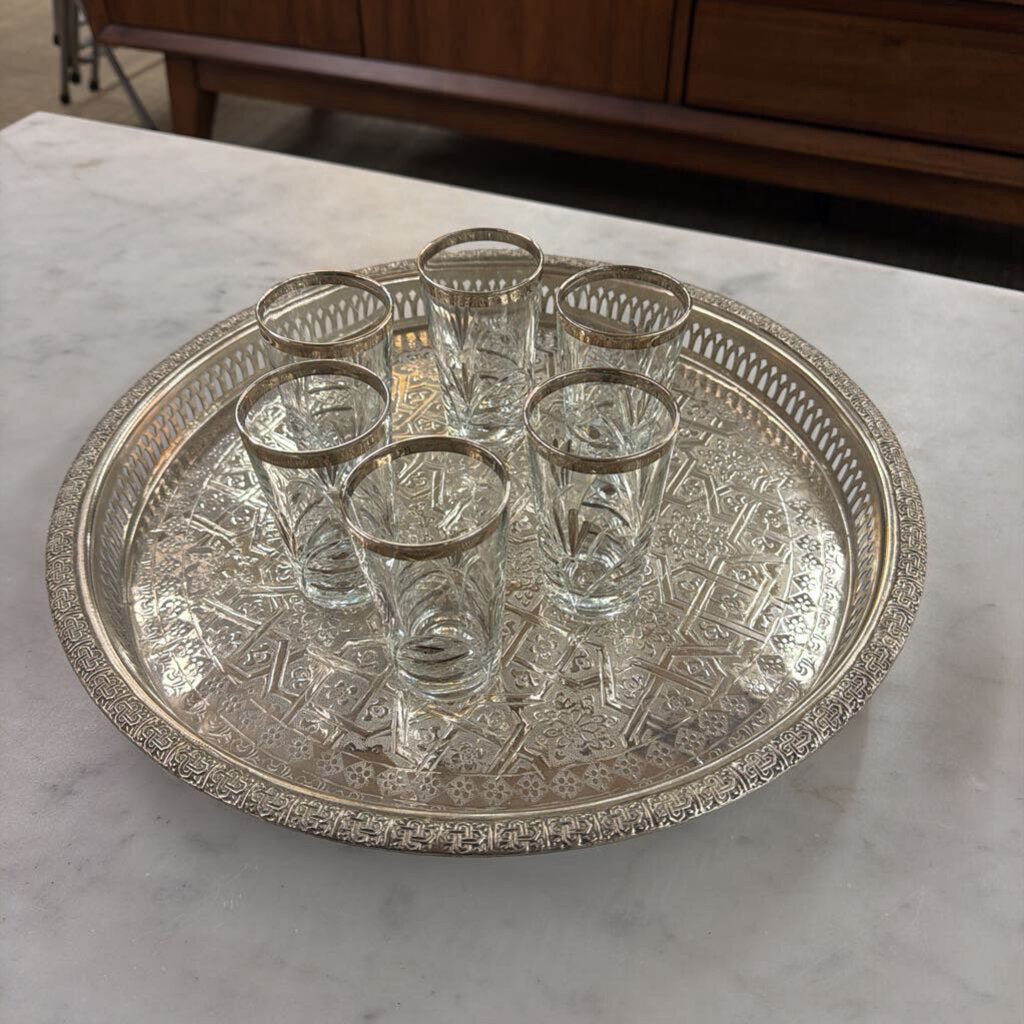 Set of six clear glasses on an ornate silver tray on a marble surface.