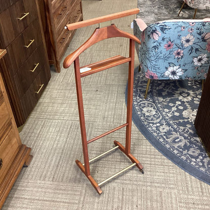 Wooden coat stand on a carpeted floor with furniture and a floral chair in the background.
