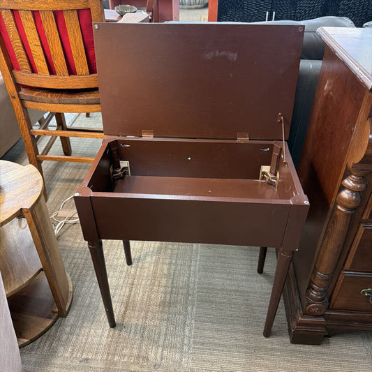 Brown sewing machine on a carpeted floor with furniture around