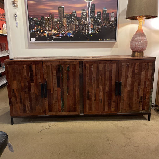 Wooden sideboard in a room with a cityscape painting and lamp.