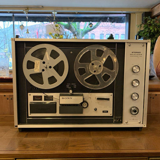 Vintage Sony reel-to-reel tape recorder on a wooden surface with a window in the background.