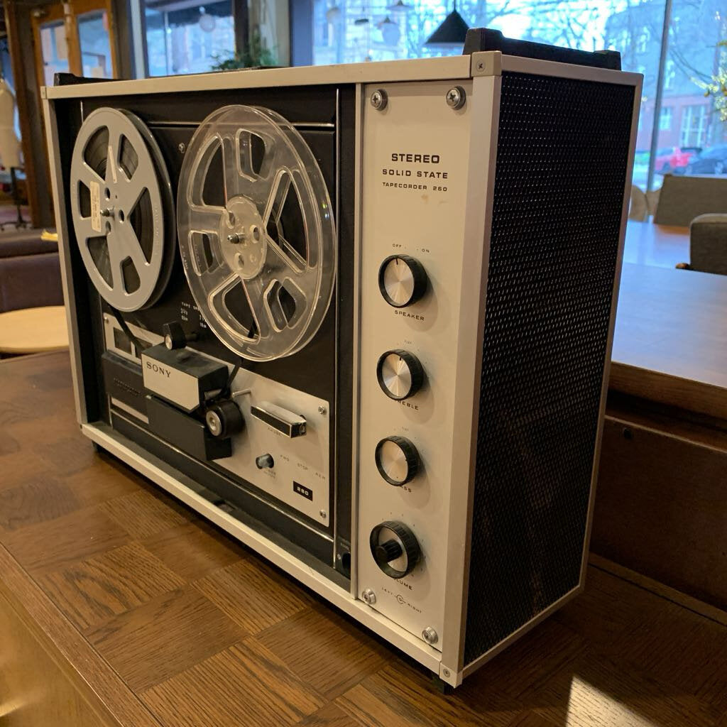 Vintage reel-to-reel tape recorder on a wooden floor with a blurred indoor background