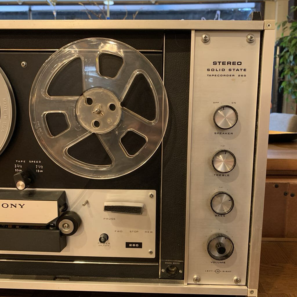 Vintage reel-to-reel tape recorder with control knobs and a large reel on a wooden surface.