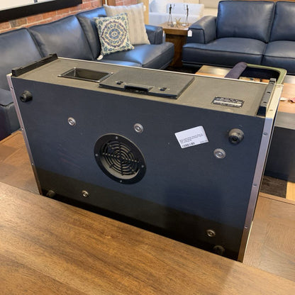 Black electronic device on a wooden surface with blue leather couches in the background