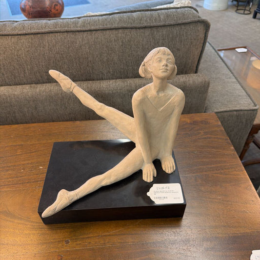 Statue of a dancer on a black base on a wooden table with a couch in the background