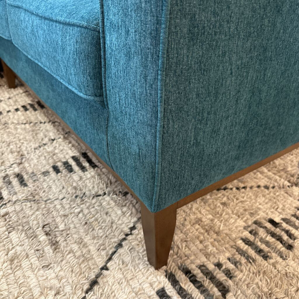 Close-up of a blue upholstered chair corner on a patterned rug