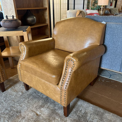 Brown leather armchair with nailhead trim in a room setting.