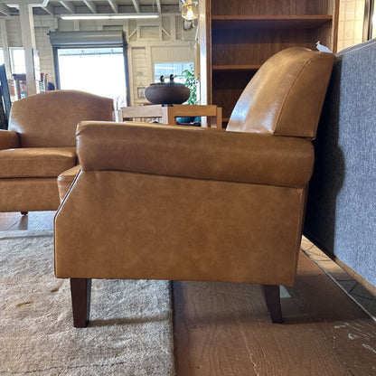 Brown leather armchair in a room with a bookshelf and other furniture.