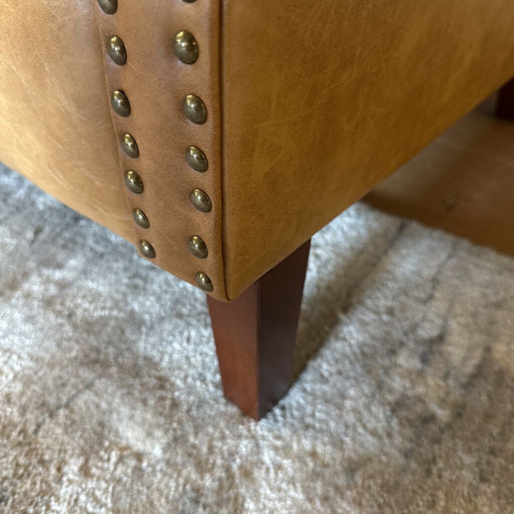 Close-up of a brown leather chair with metal studs on a carpeted floor.