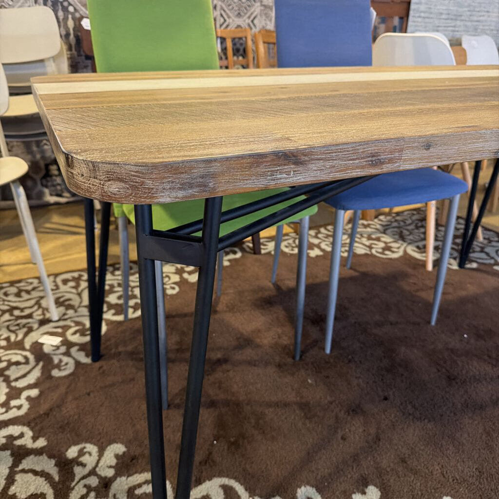 Wooden dining table with black metal legs in a room with chairs and a patterned rug.