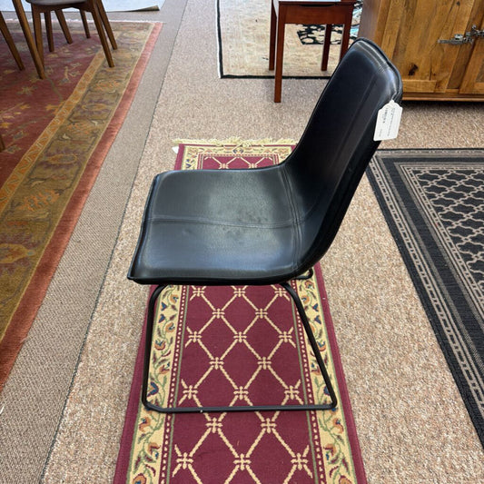 Black chair on a patterned rug with a wooden cabinet in the background