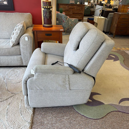 Gray recliner chair in a furniture store setting with other furniture items in the background.