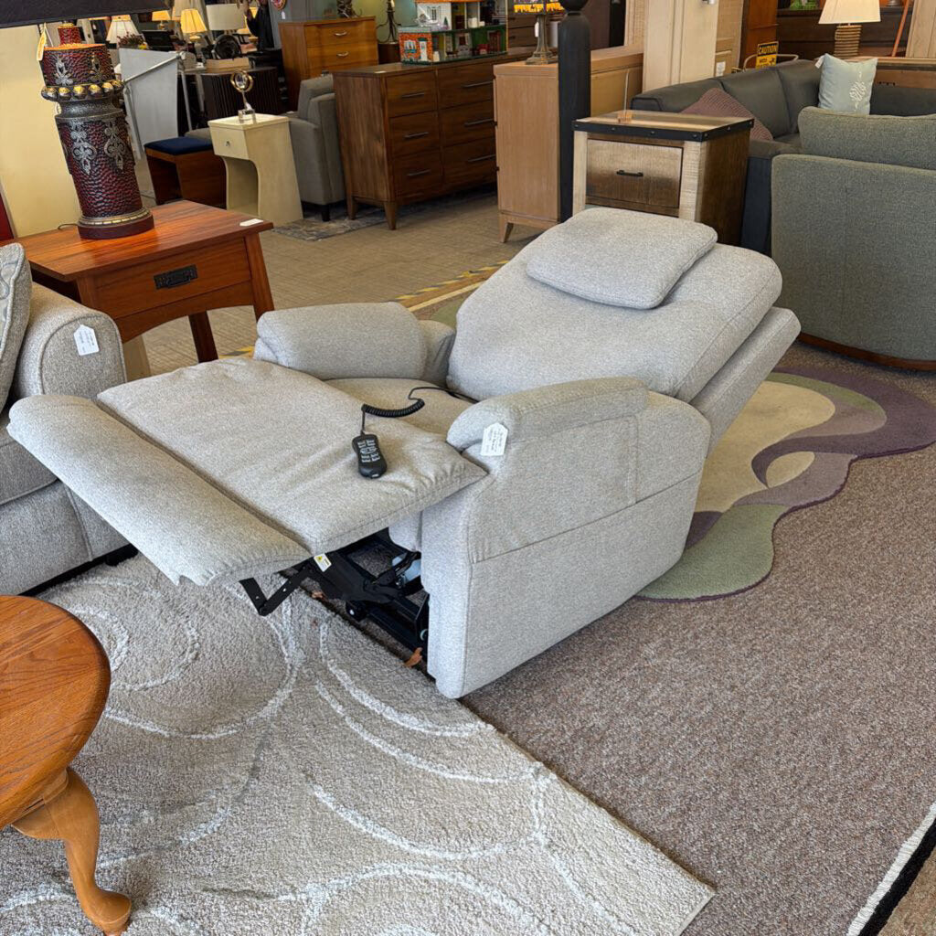 Gray recliner chair with cup holder and remote control in a furniture store setting.
