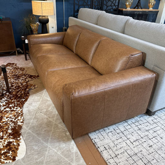Brown leather sofa in a living room setting with a cowhide rug and patterned rug.