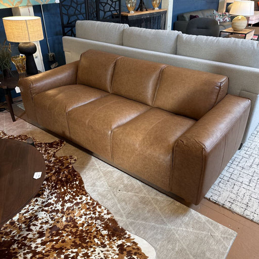 Brown leather sofa in a room with a cowhide rug and other furniture.