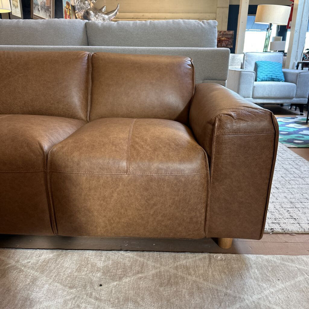 Brown leather sofa in a living room setting with a gray couch and colorful rug.