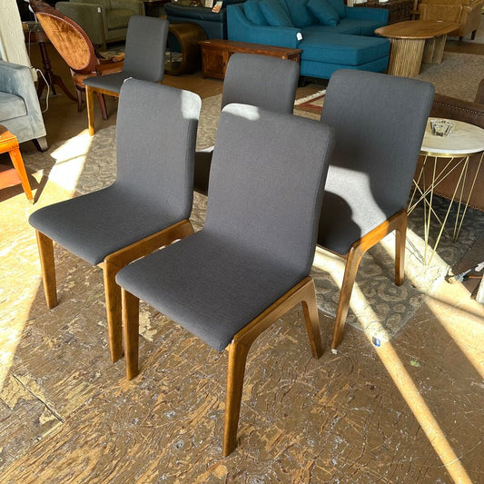 Four gray chairs with wooden legs on a textured floor.