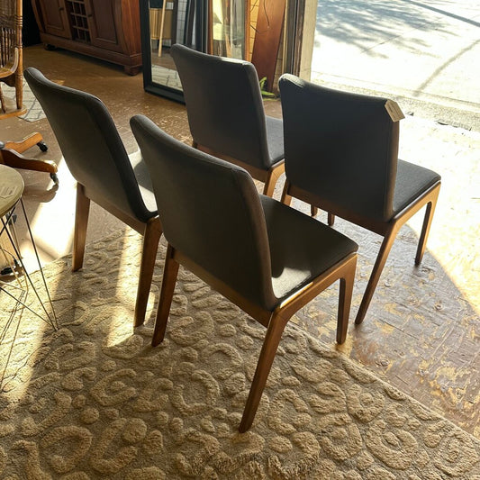 Four dark brown chairs on a textured rug with a window in the background