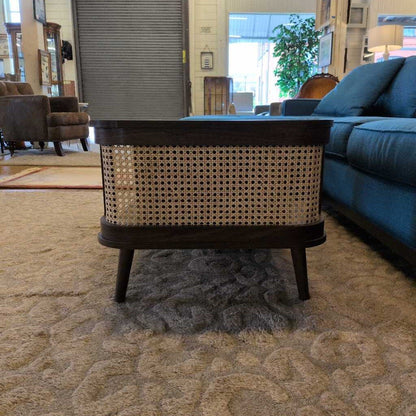 Wicker side table in a living room setting with a blue sofa and decorative items.