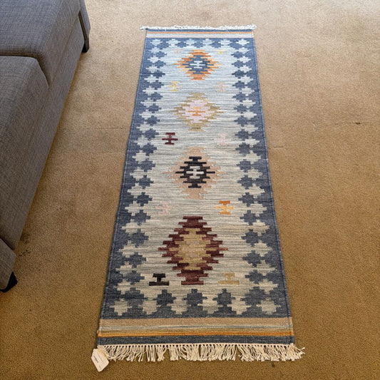 Patterned rug on a carpeted floor next to a gray sofa.