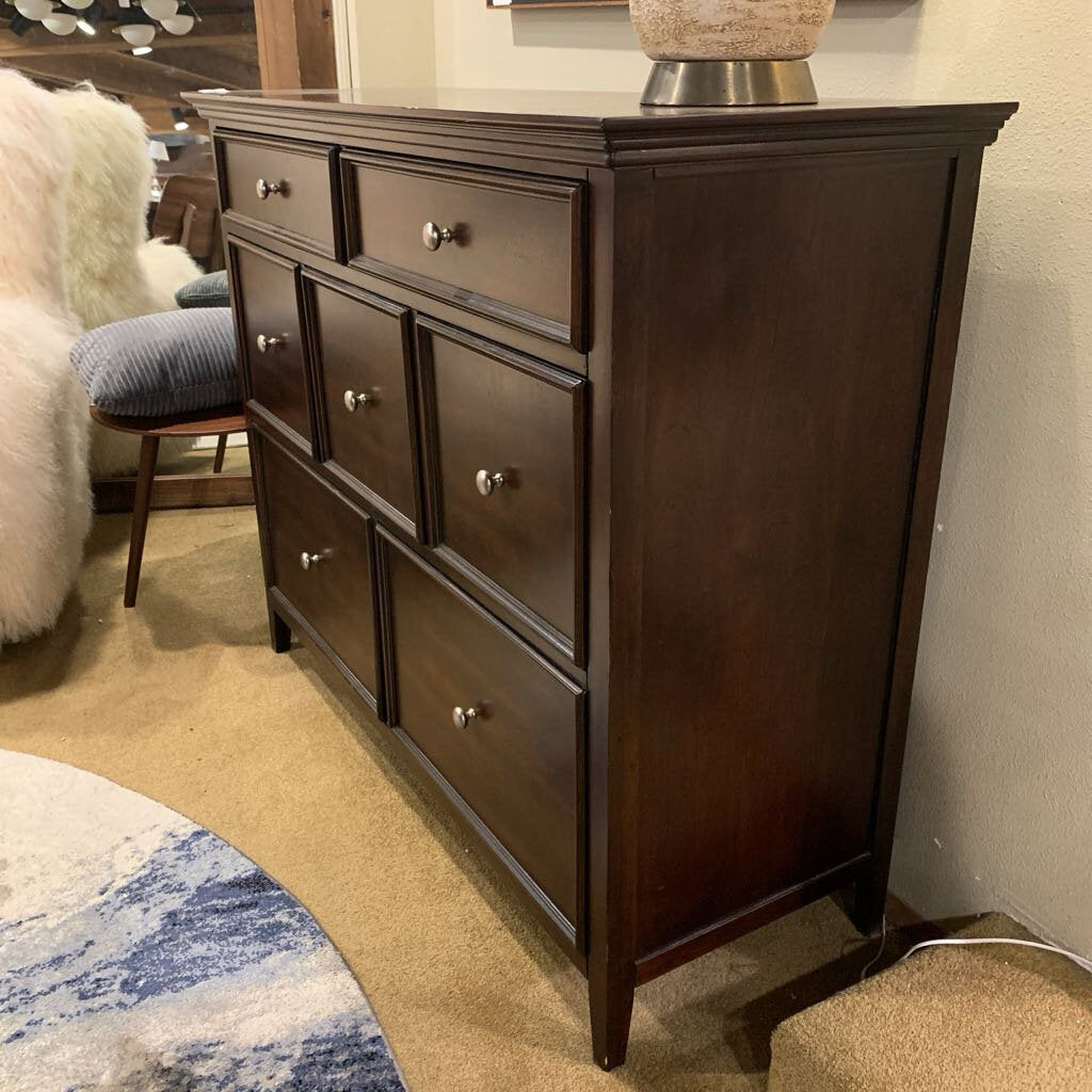 Dark wood dresser with multiple drawers in a room setting.