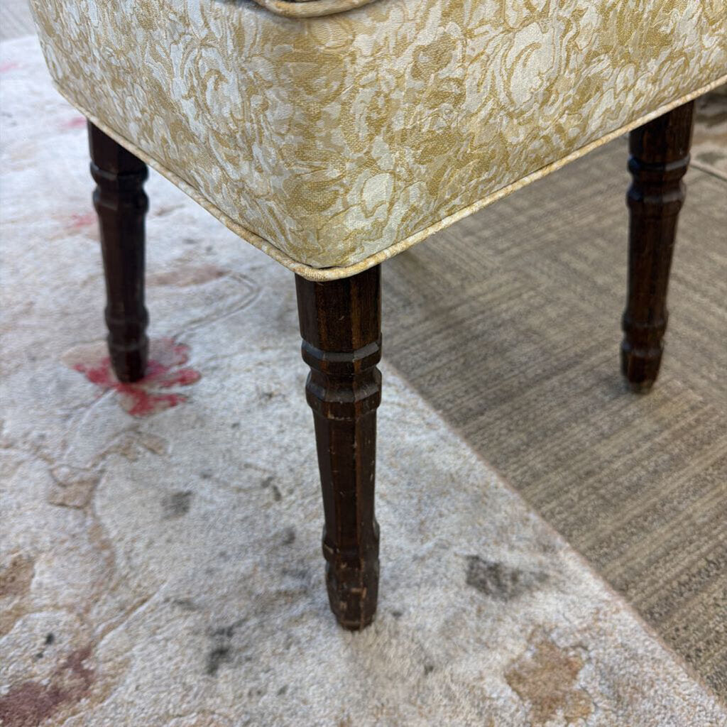 Close-up of a chair with patterned fabric and dark wooden legs on a textured floor.