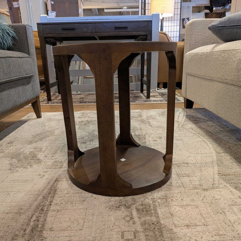 Wooden side table in a furniture store setting with chairs and other tables in the background.