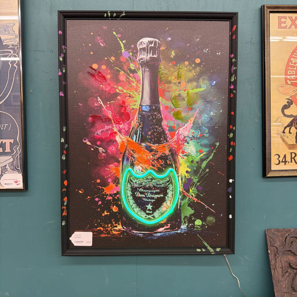 Framed artwork of a champagne bottle with colorful splashes on a teal wall.