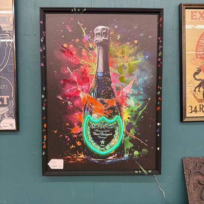 Framed artwork of a champagne bottle with colorful splashes on a teal wall.