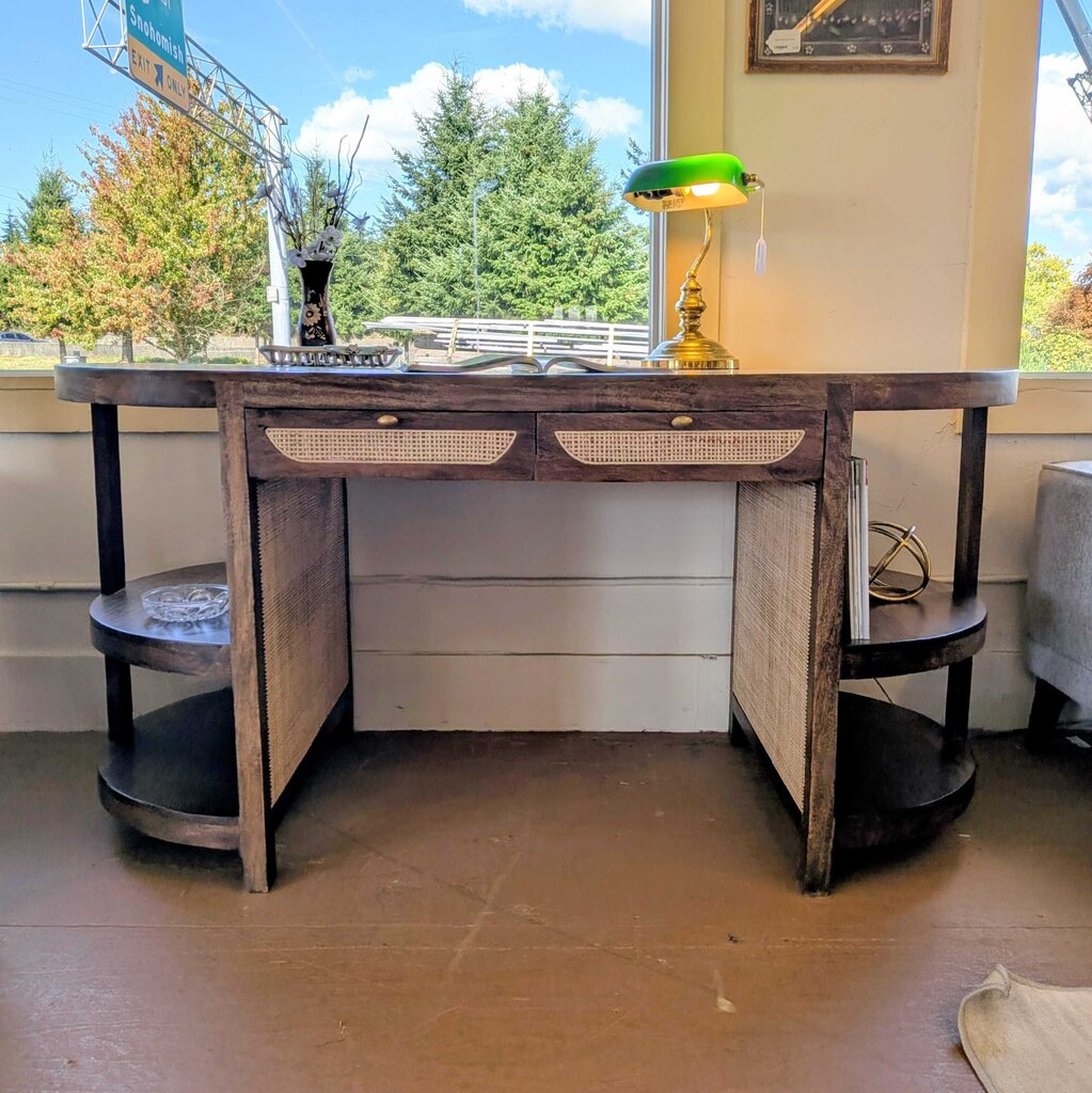 Wooden desk with drawers and shelves in a room with large windows.