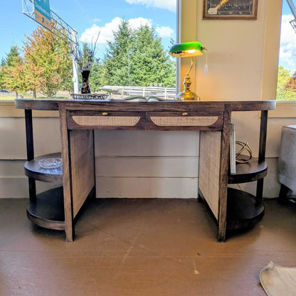 Wooden desk with drawers and shelves in a room with large windows.