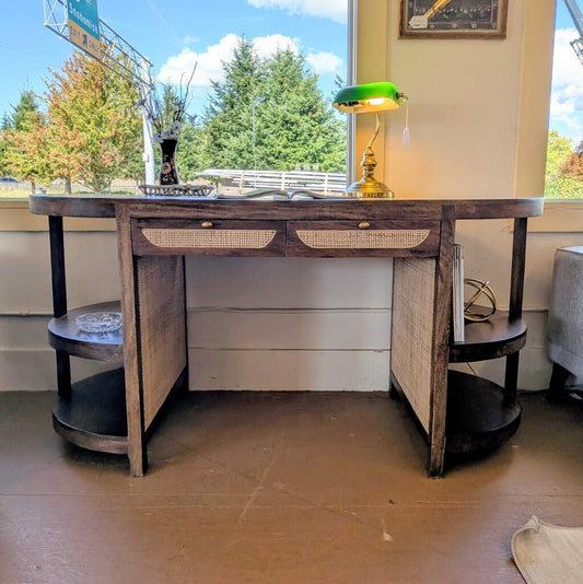 Wooden desk with drawers and shelves in a room with large windows.