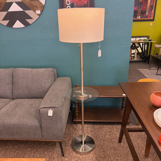 Floor lamp with a beige shade in a room with a gray sofa and wooden table.