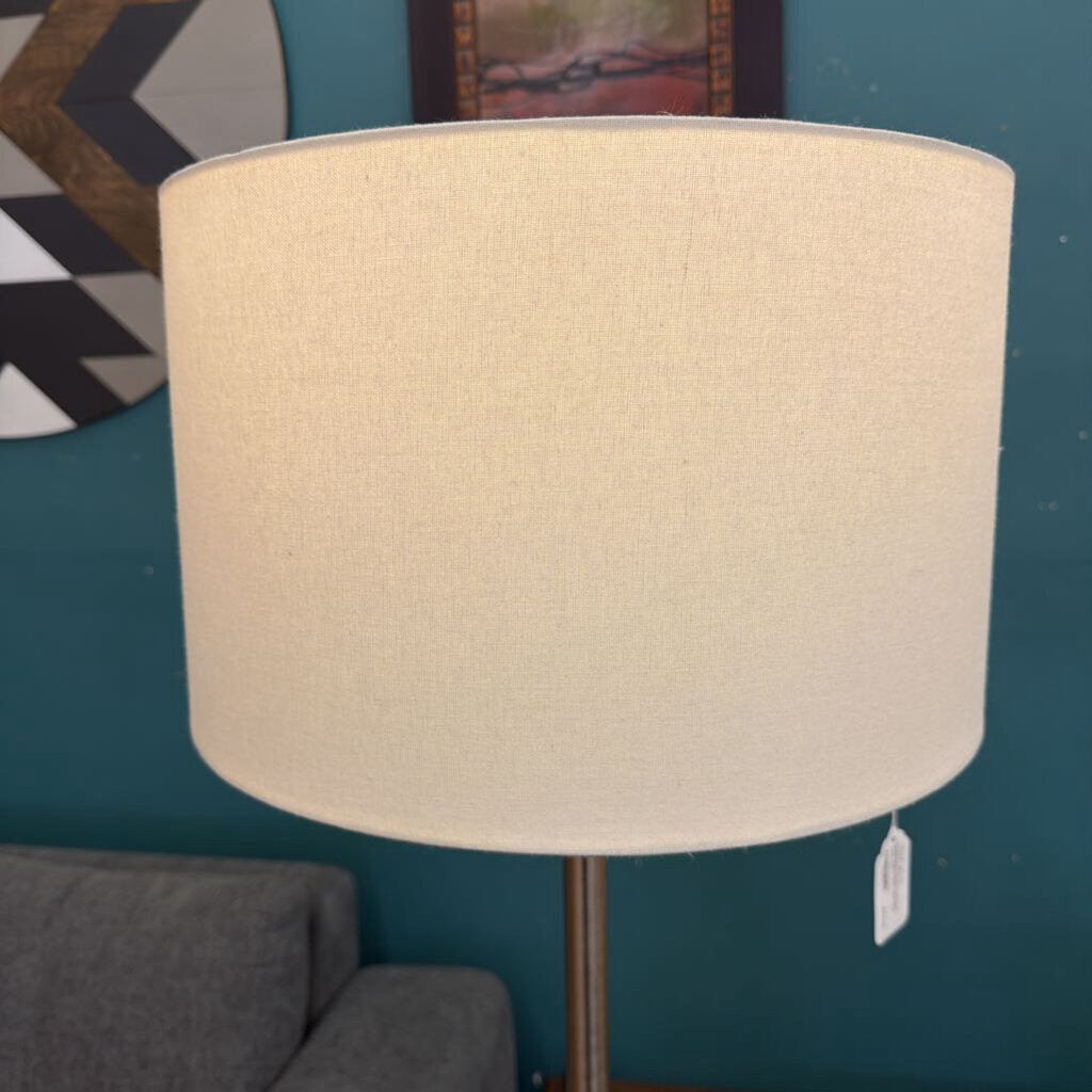 Beige lampshade on a stand against a teal wall with decorative items.