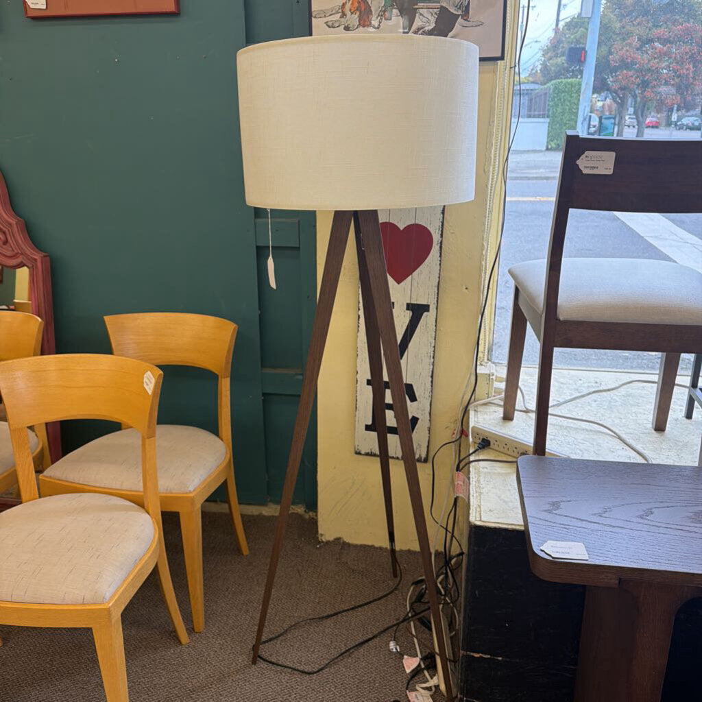 Tall floor lamp with a beige shade in a room with chairs and a green wall.