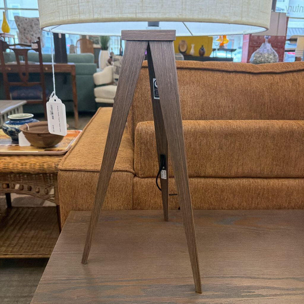 Wooden floor lamp with a beige lampshade in a room with furniture and decor.