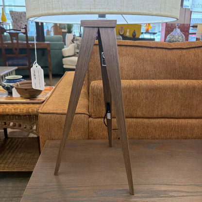 Wooden floor lamp with a beige lampshade in a room with furniture and decor.