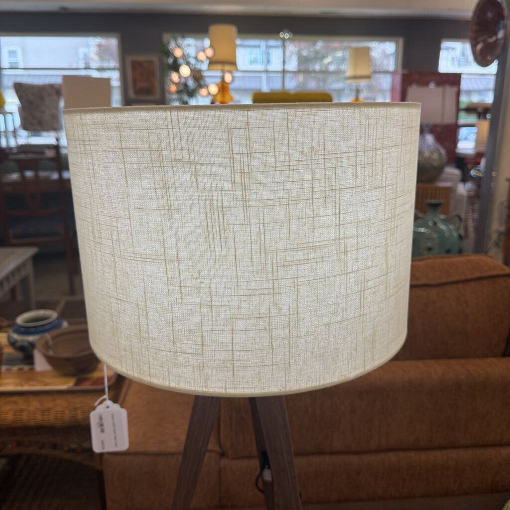 Wooden floor lamp with a beige lampshade in a room with furniture and decor.