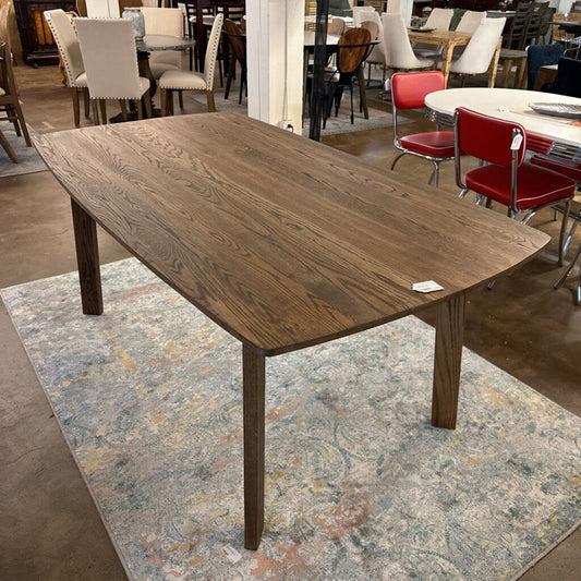 Wooden dining table on a patterned rug with a blurred background of chairs and tables.