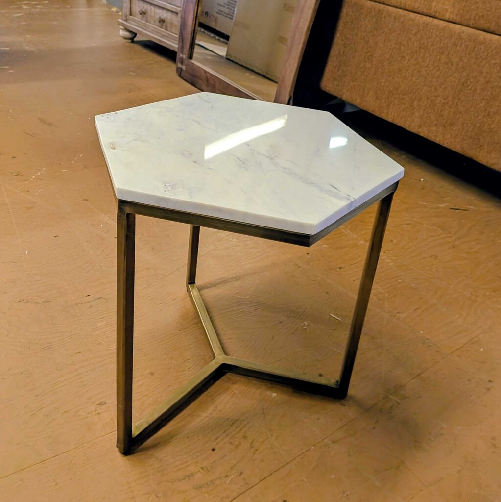 Hexagonal marble side table with black metal legs on a wooden floor.