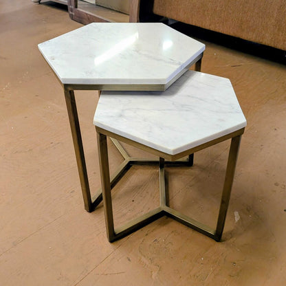 Hexagonal marble top tables with brass frames on a wooden floor.