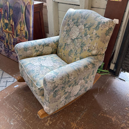 Floral-patterned armchair on a wooden floor with a colorful box in the background