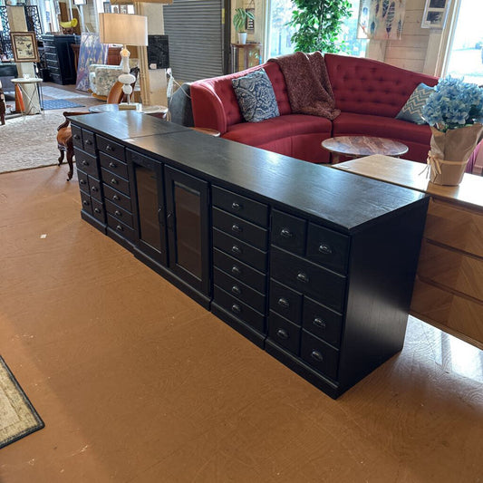 Long black dresser in a living room with a red sofa and decorative items.