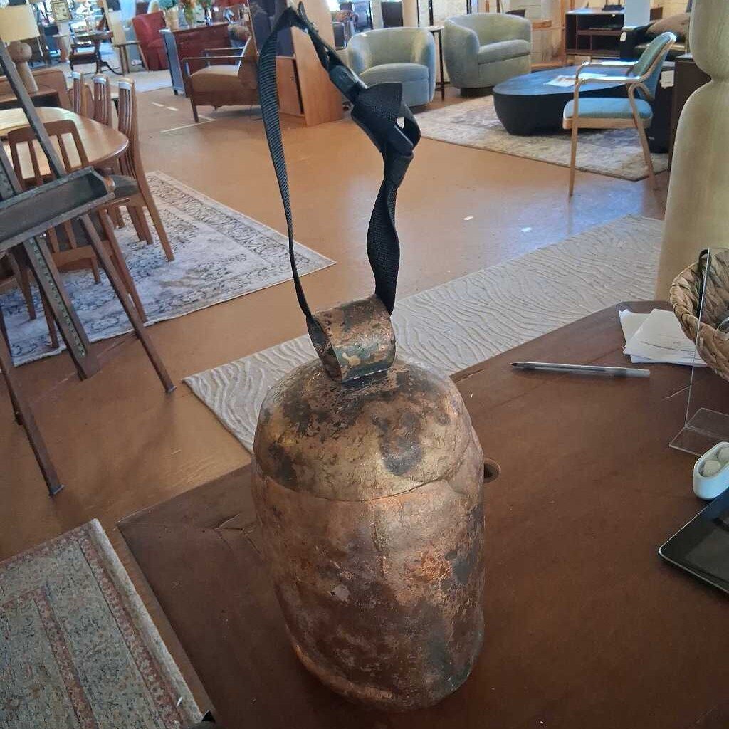 Rust-colored bell with a black rope on a wooden table in a room with furniture and decor.