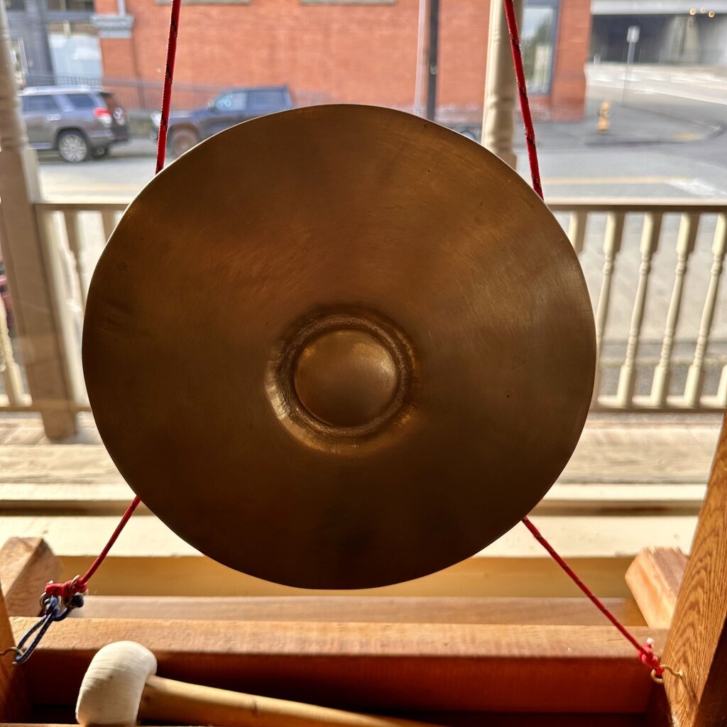 Bronze gong on a stand with a red string, outdoors.