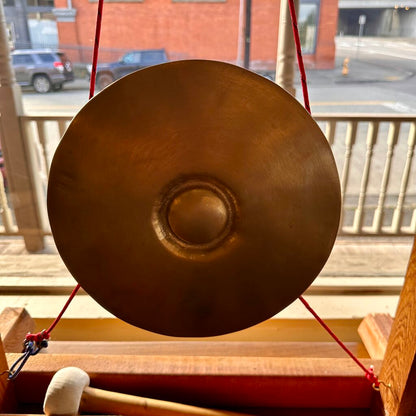 Bronze gong on a stand with a red string, outdoors.