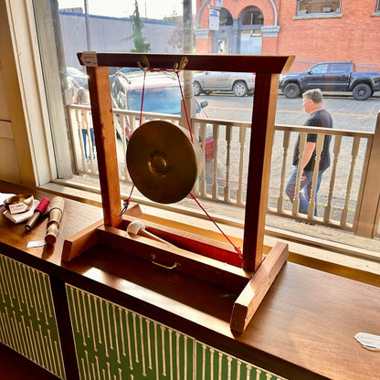 Wooden gong on a stand with a street view outside a window in the background