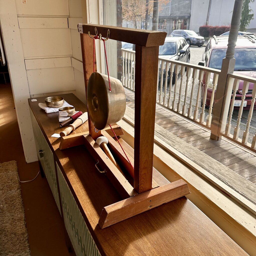 Wooden gong stand with gongs on a wooden surface near a window.